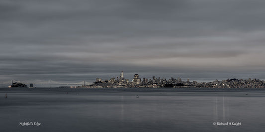 Nightfall’s Edge by Richard H Knight: San Francisco’s illuminated skyline, Alcatraz and the Bay Bridge across calm bay waters beneath a clouded evening sky