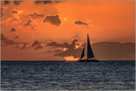 Sailboat on the ocean during sunset with an orange sky and clouds.