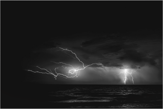 Black and white image of a dramatic lightning strike over water.