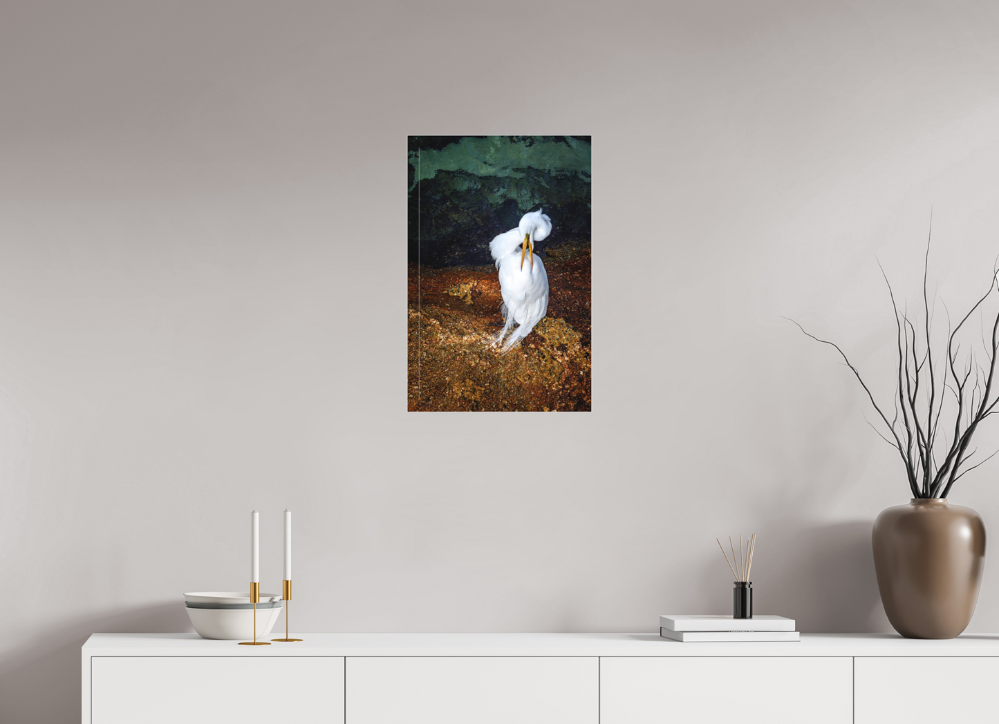 Framed photograph of a white bird on a wall above a white cabinet with decorative items.