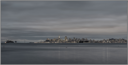 Nightfall's Edge — San Francisco skyline at dusk from Sausalito, early city lights glowing beneath a heavy overcast sky with the Bay Bridge fading into the mist, framed color fine art photography print by Richard H Knight