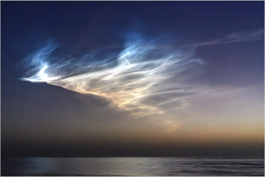 Noctilucent clouds over a body of water at dawn's early light