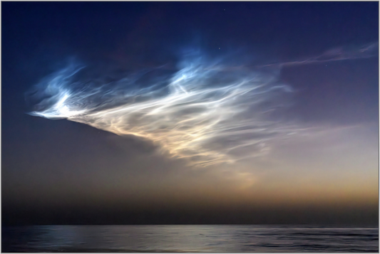 Noctilucent clouds over a body of water at dawn's early light