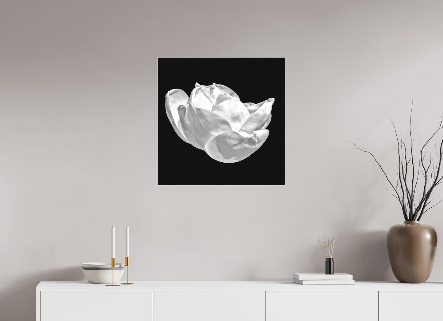 Framed black and white abstract art piece on a wall above a white cabinet with decorative items.