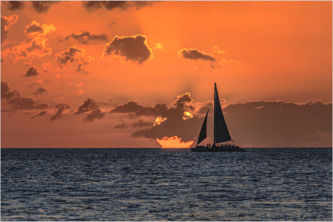 Sailboat on the water with a dramatic orange sunset sky