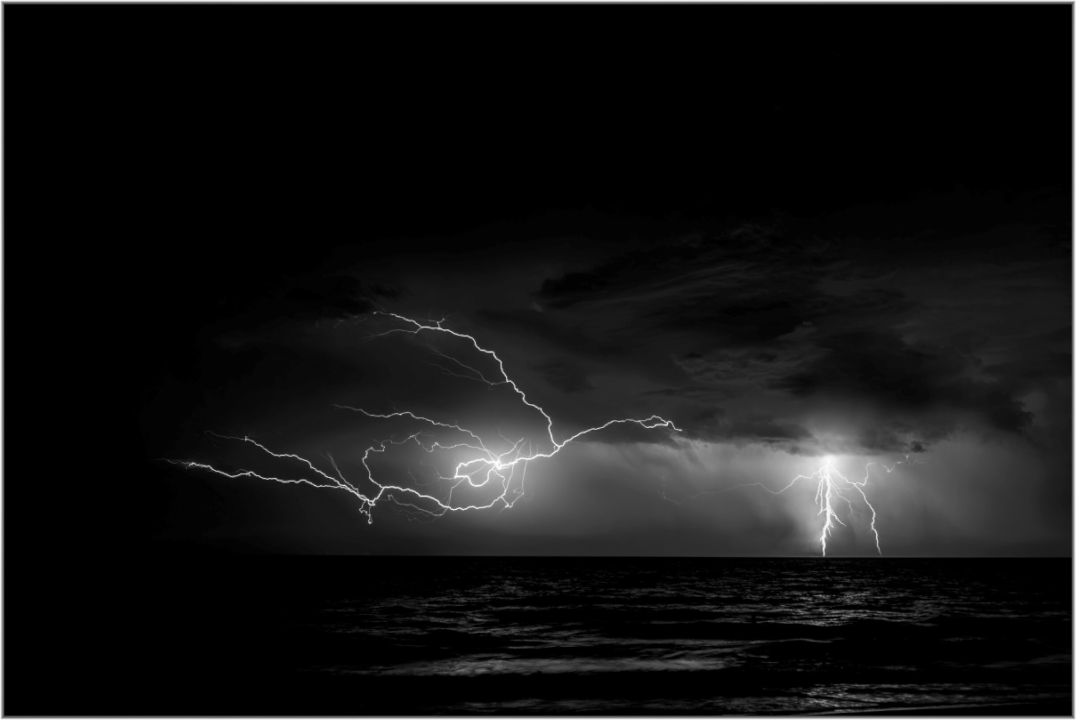 Black and white image of lightning strikes over water