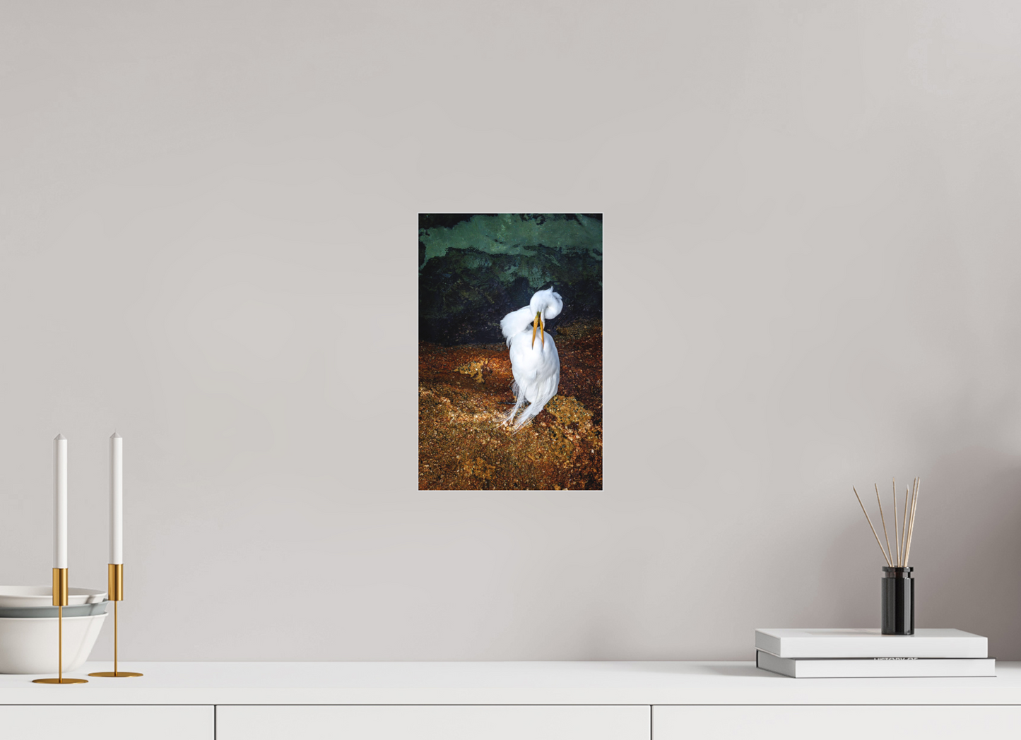 Framed photograph of a white bird on a wall above a white surface with decorative items.