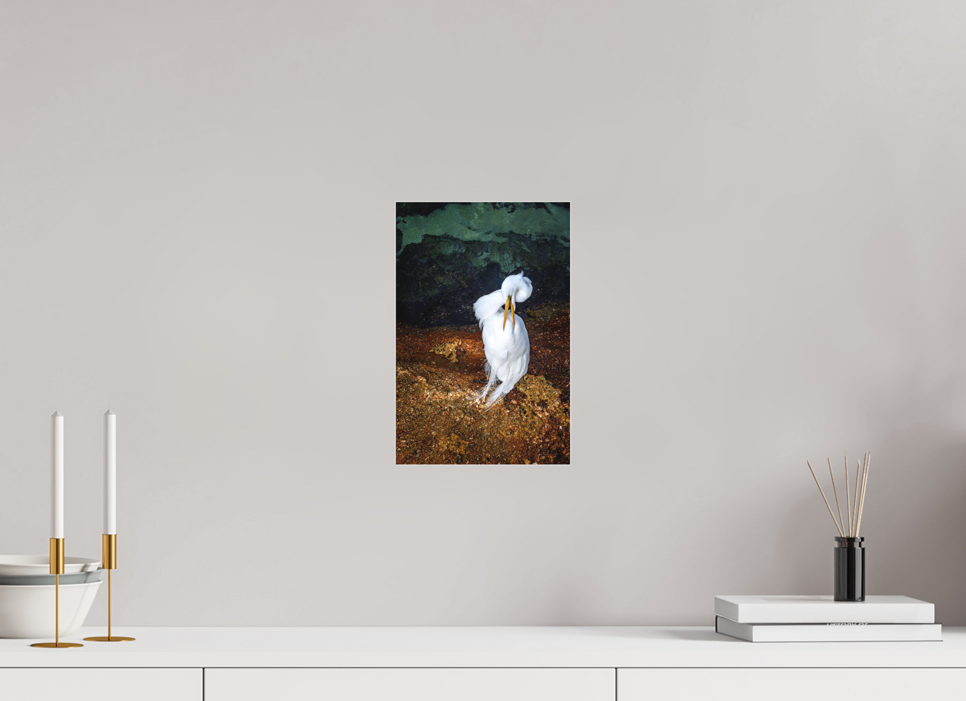 Framed photograph of a white bird on a wall above a white surface with decorative items.